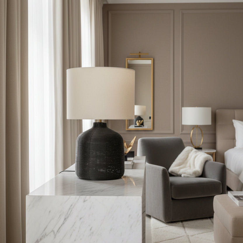 Table lamp with textured black base and beige shade on a white background