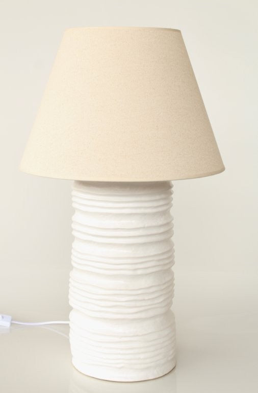 Table lamp with a textured white base and beige lampshade on a plain background