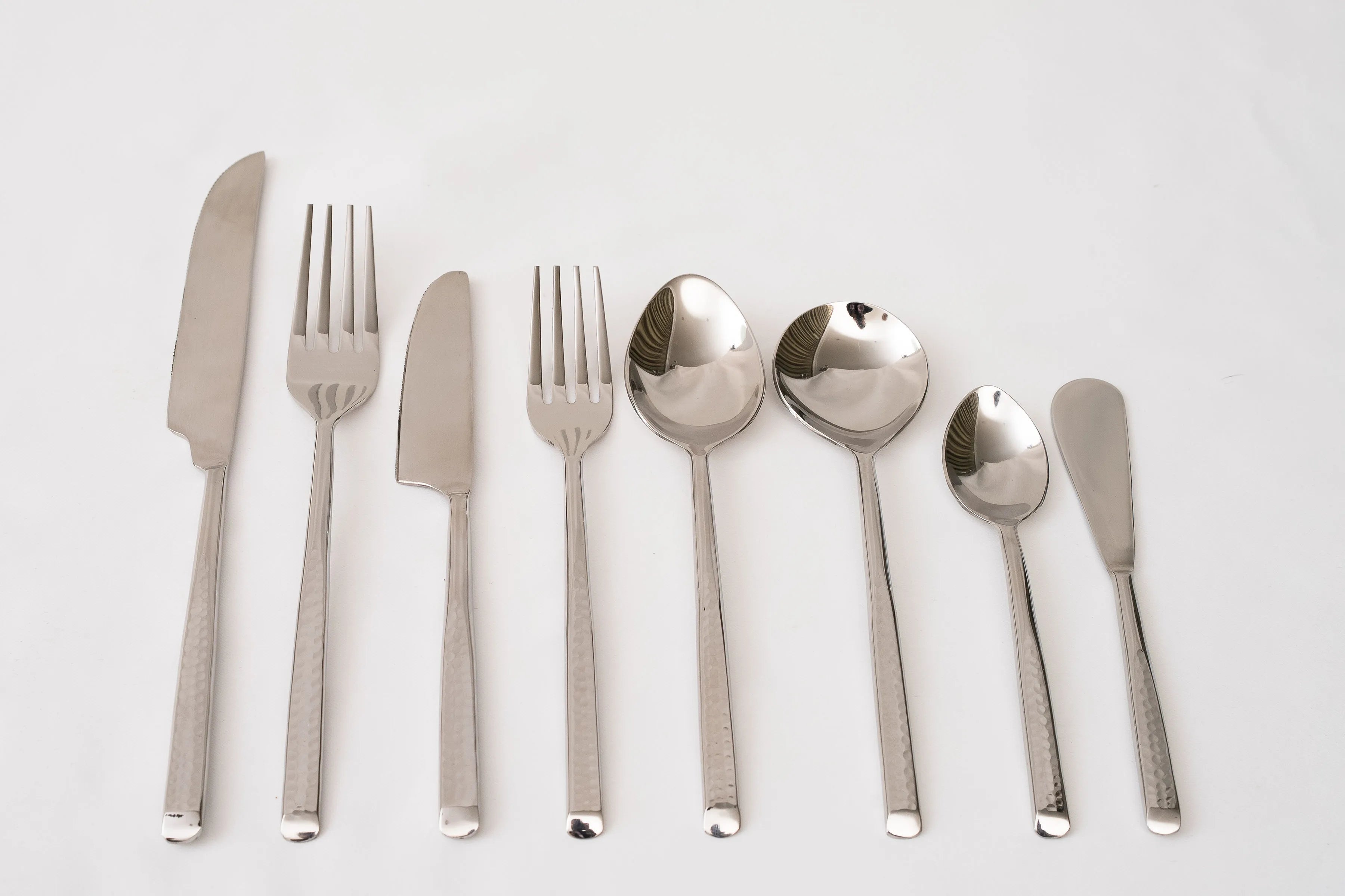 Set of silver cutlery including knives, forks, and spoons on a light gray background