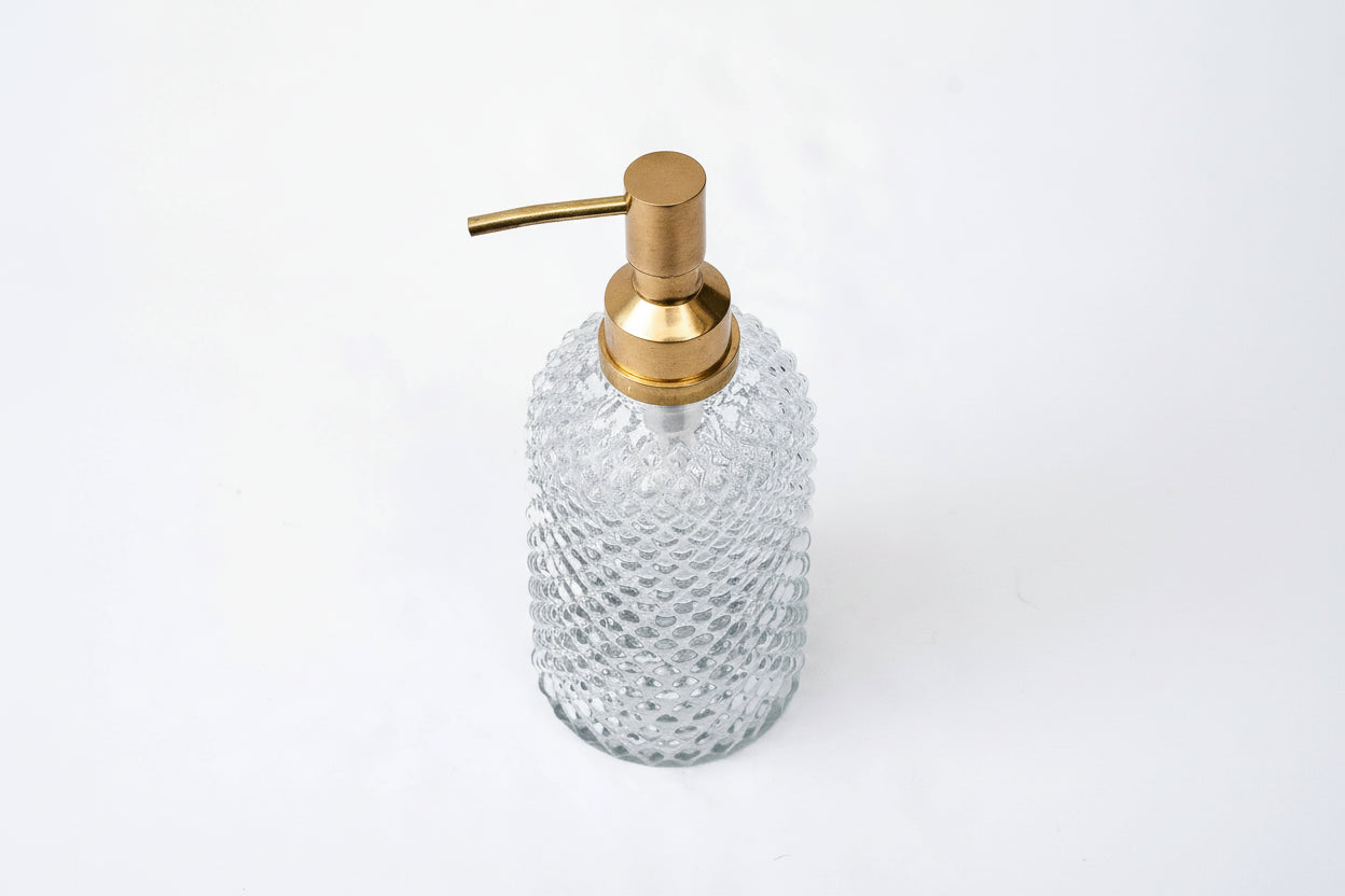 Glass soap dispenser with gold pump on a white background