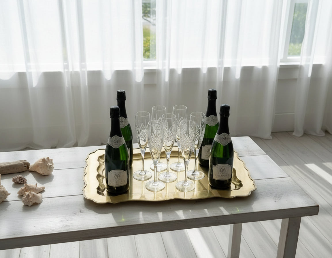 Four bottles of champagne and six glasses on a gold tray with a white background