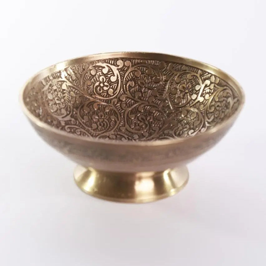 Decorative brass bowl with intricate patterns on a white background