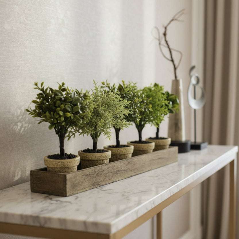 Five artificial plants in woven pots on a wooden tray against a plain background
