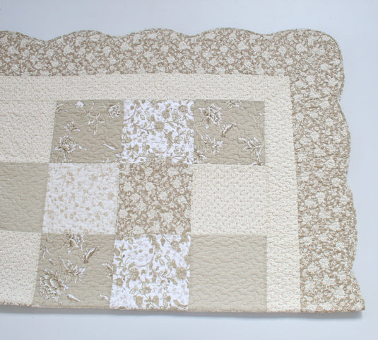 A square quilted textile with a patchwork design in beige, cream, and white floral patterns, finished with a scalloped border, shown on a plain light background.