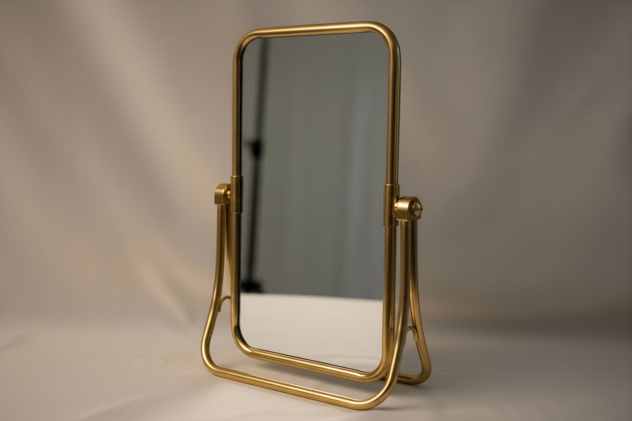Gold-framed mirror on a white surface with a blurred background