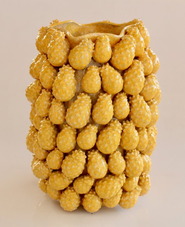 Vase with a textured surface resembling yellow berries on a beige background