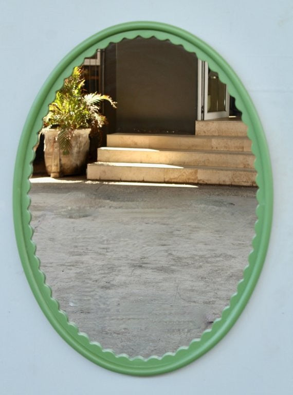 Oval mirror with a green frame on a light blue wall, reflecting steps and plants.
